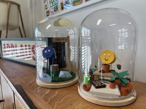 Two paper shape characters staged inside domed jars on display. 